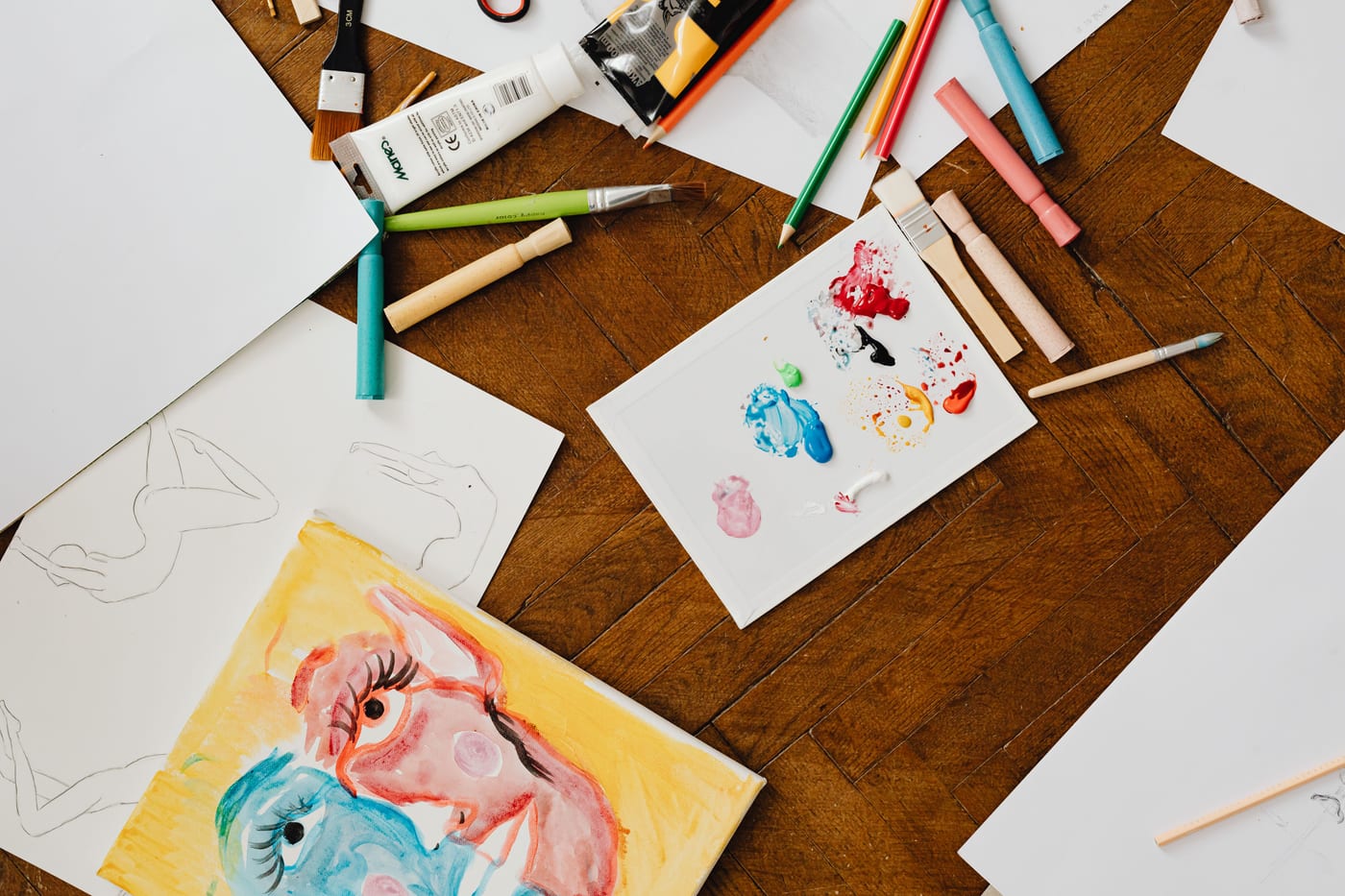 Crayones, pinceles y un dibujo hecho por un niño sobre un piso de madera